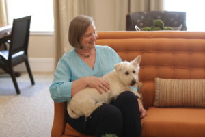 Woman sitting with therapy dog in The Gardens Memory Care