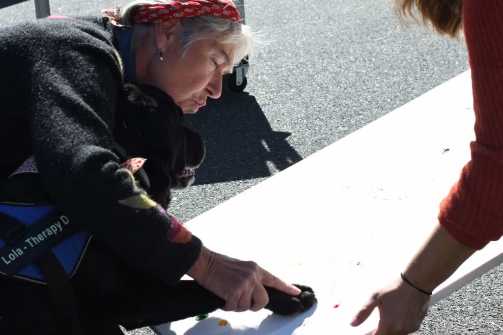 A woman helping a black Lab press its pawprint onto a canvas