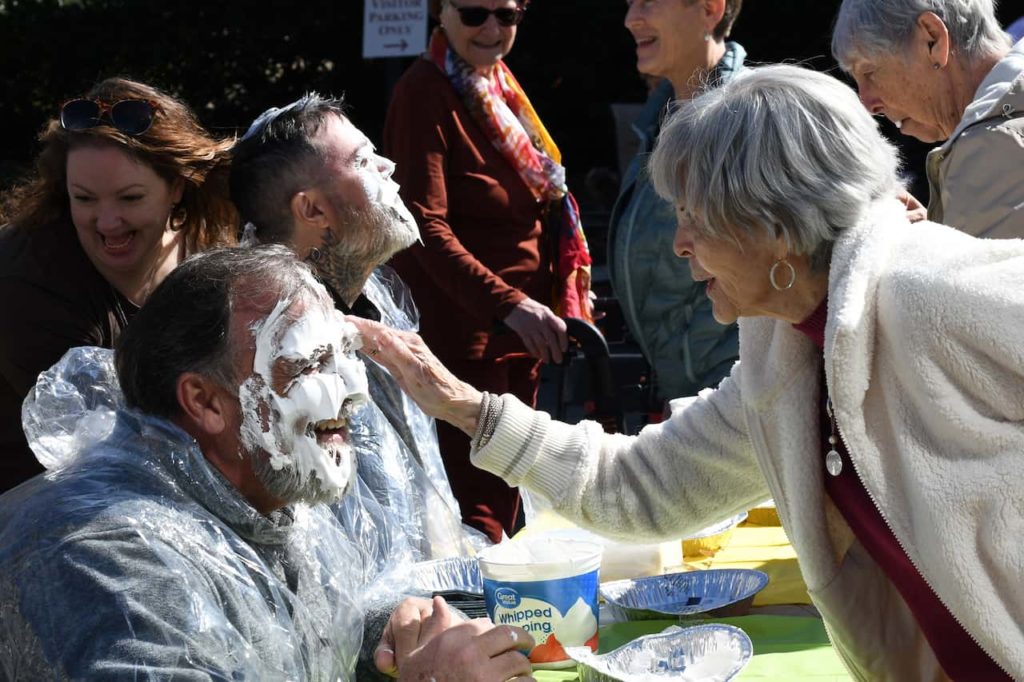 Many people laughing as a woman rubs pie cream onto man's forehead