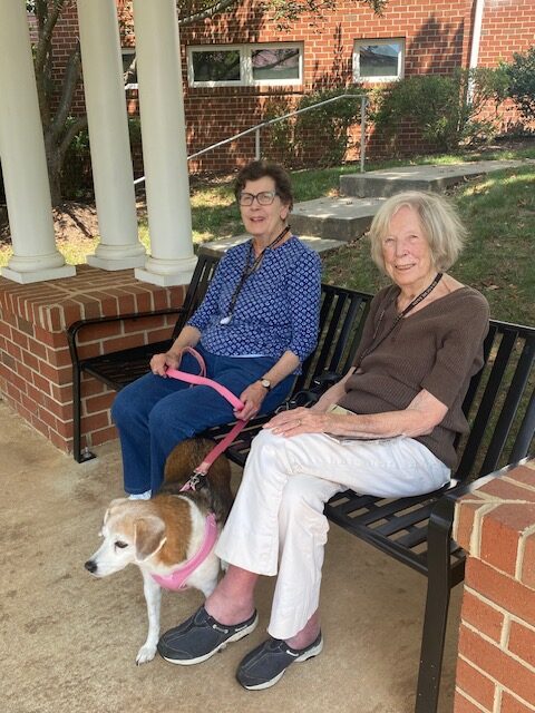 Carol and her dog Honey seated on a bench outdoors with their friend Marianne.