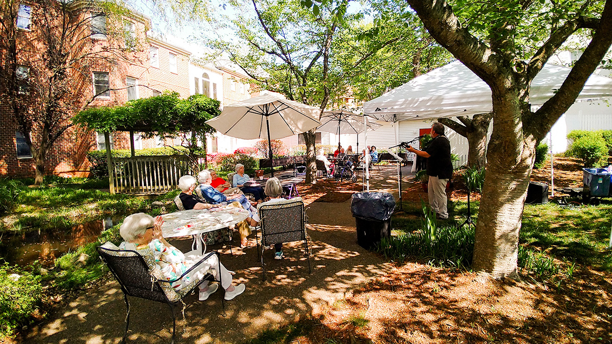 An outdoor guitar performance in the shade of trees and umbrellas at Branchlands.