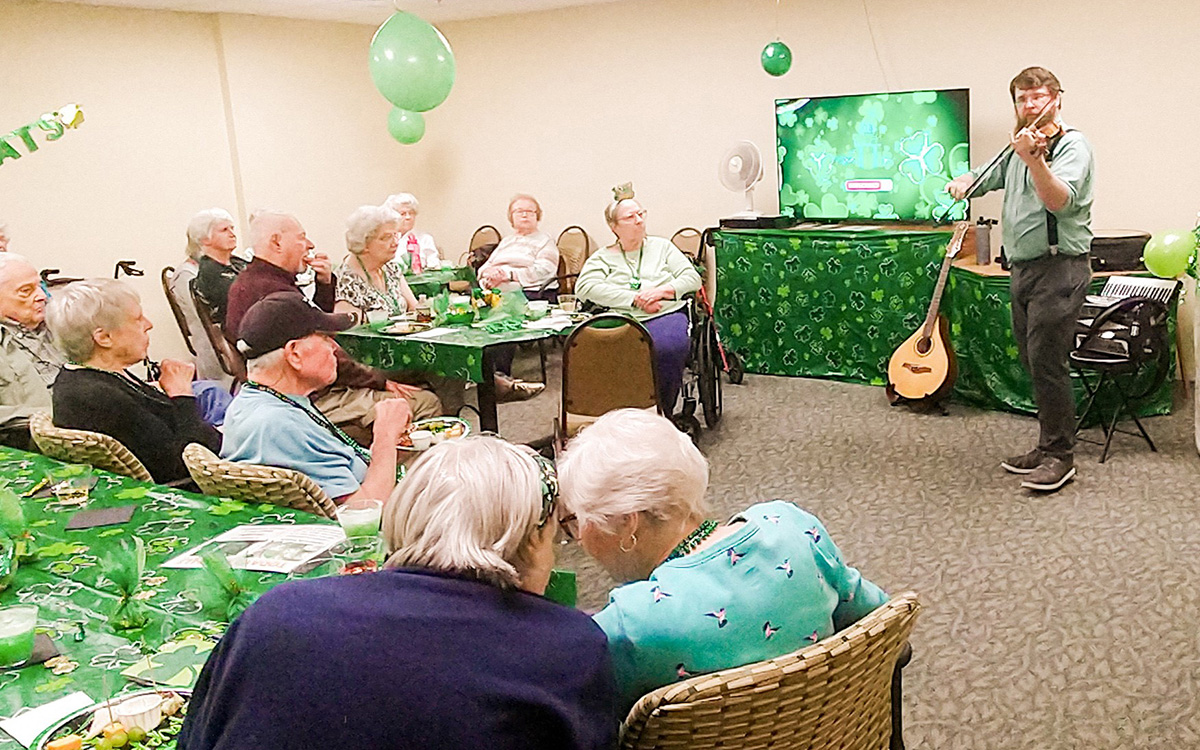 A musician playing violin for senior living residents during a St. Patrick's Day celebration.