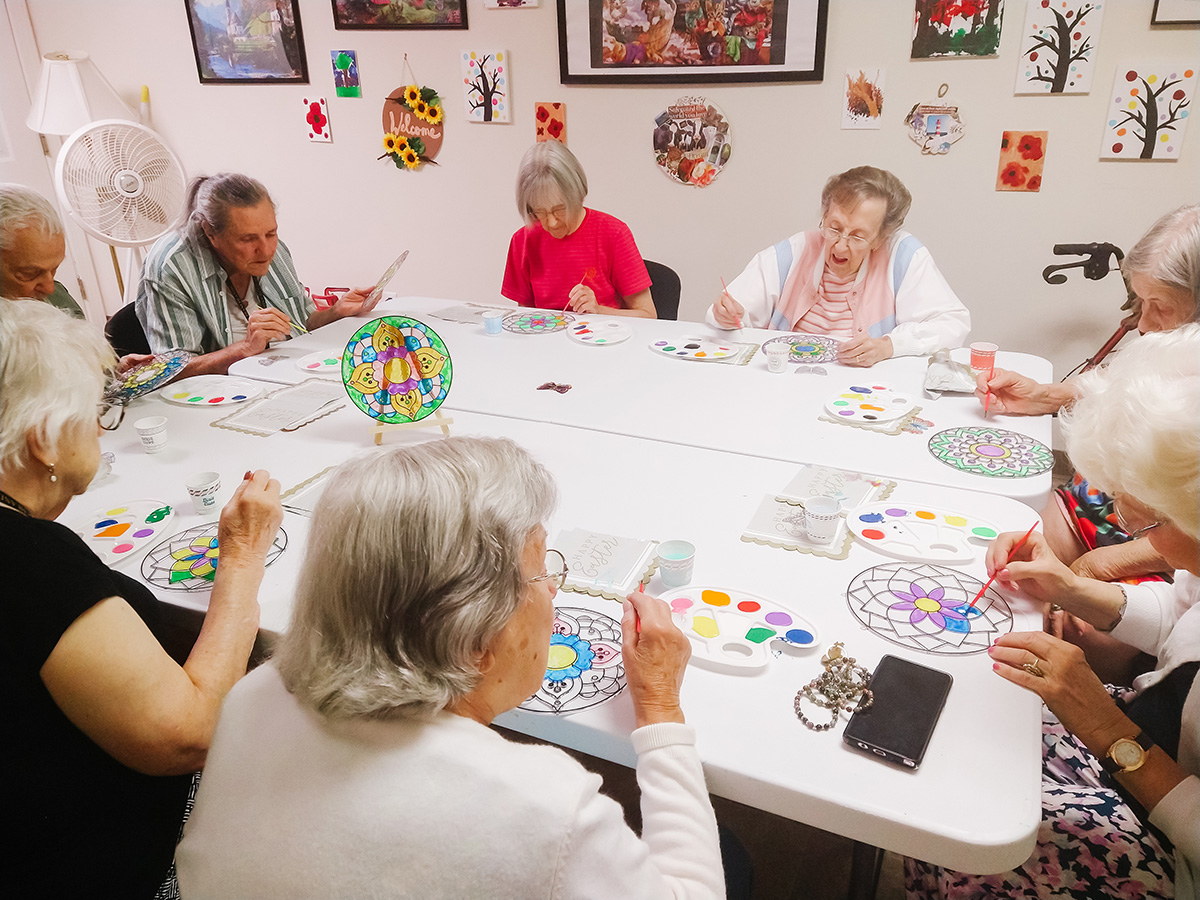 Senior living residents painting colors onto suncatchers.