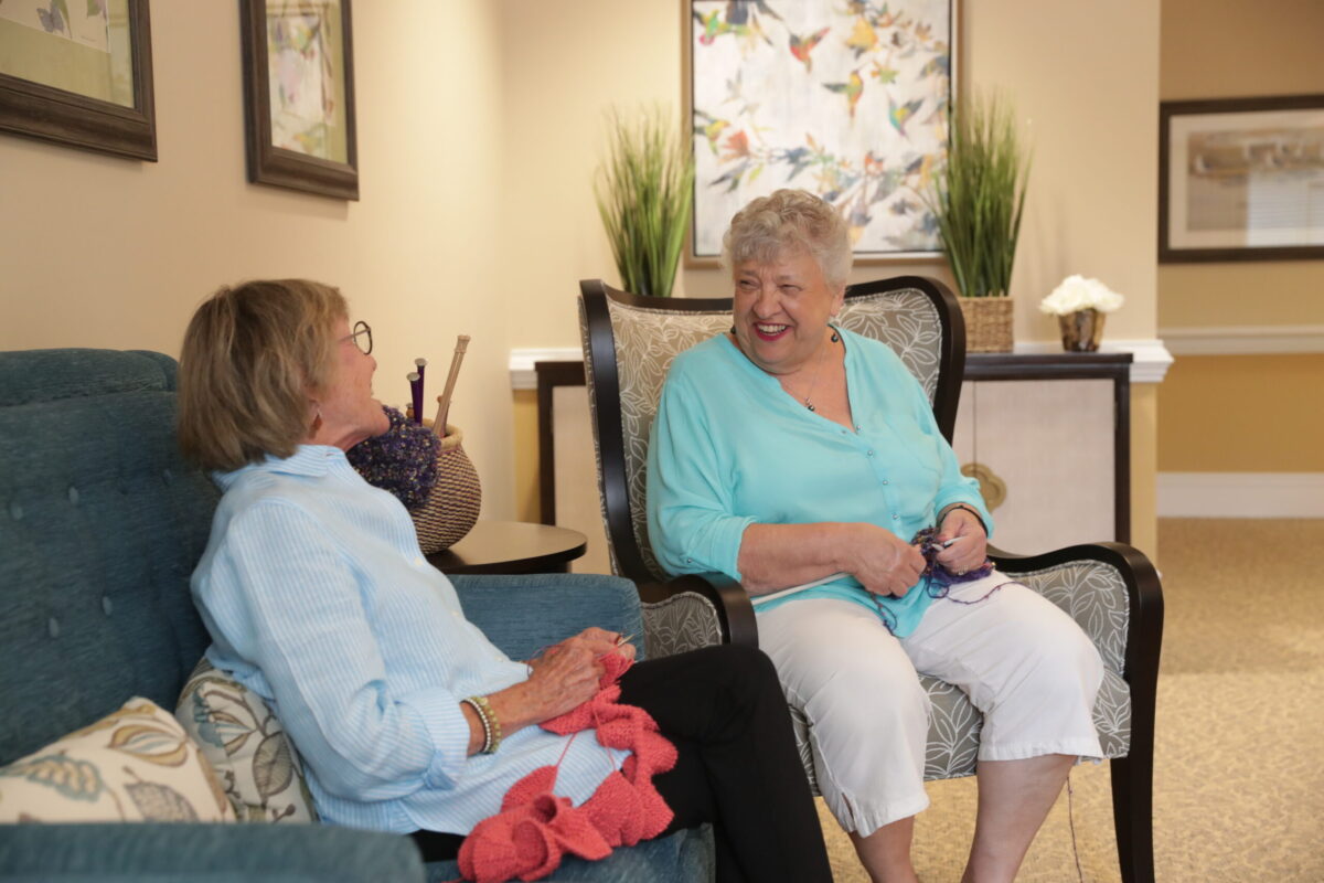 Senior living residents seated and chatting while knitting.