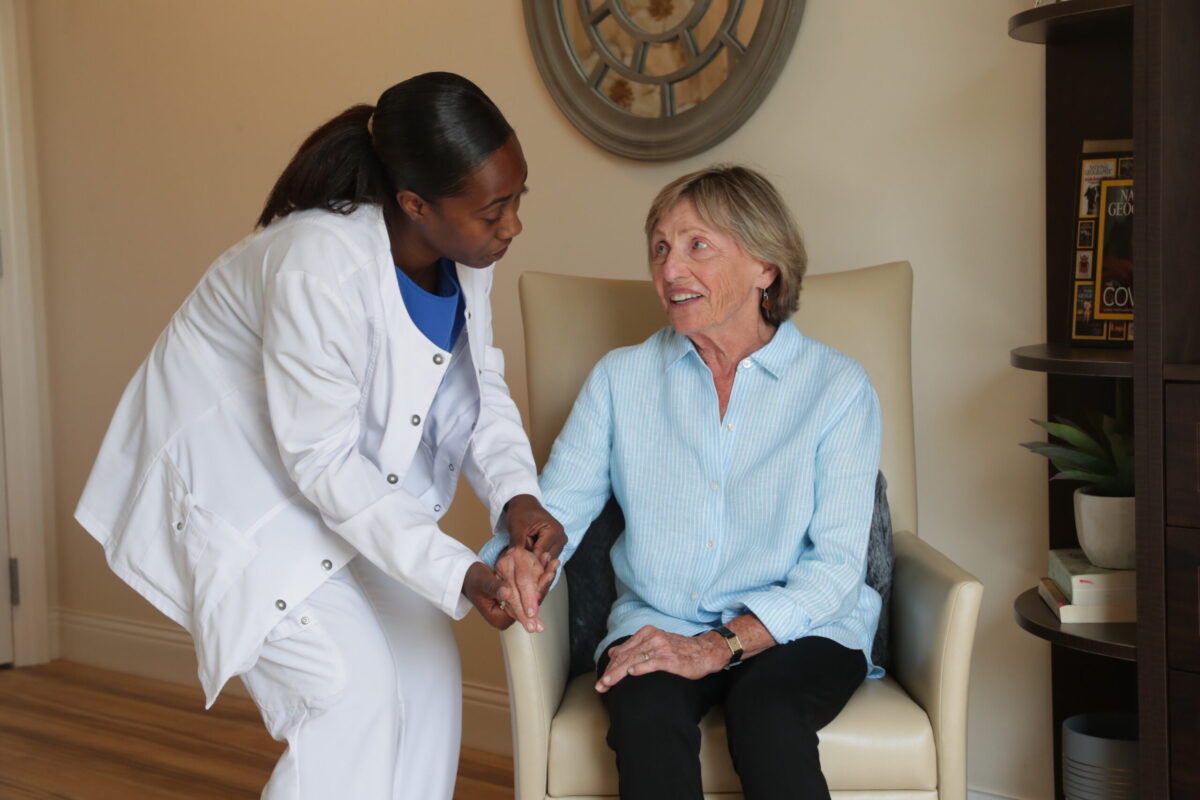 A nurse and a senior living resident in a chair talking